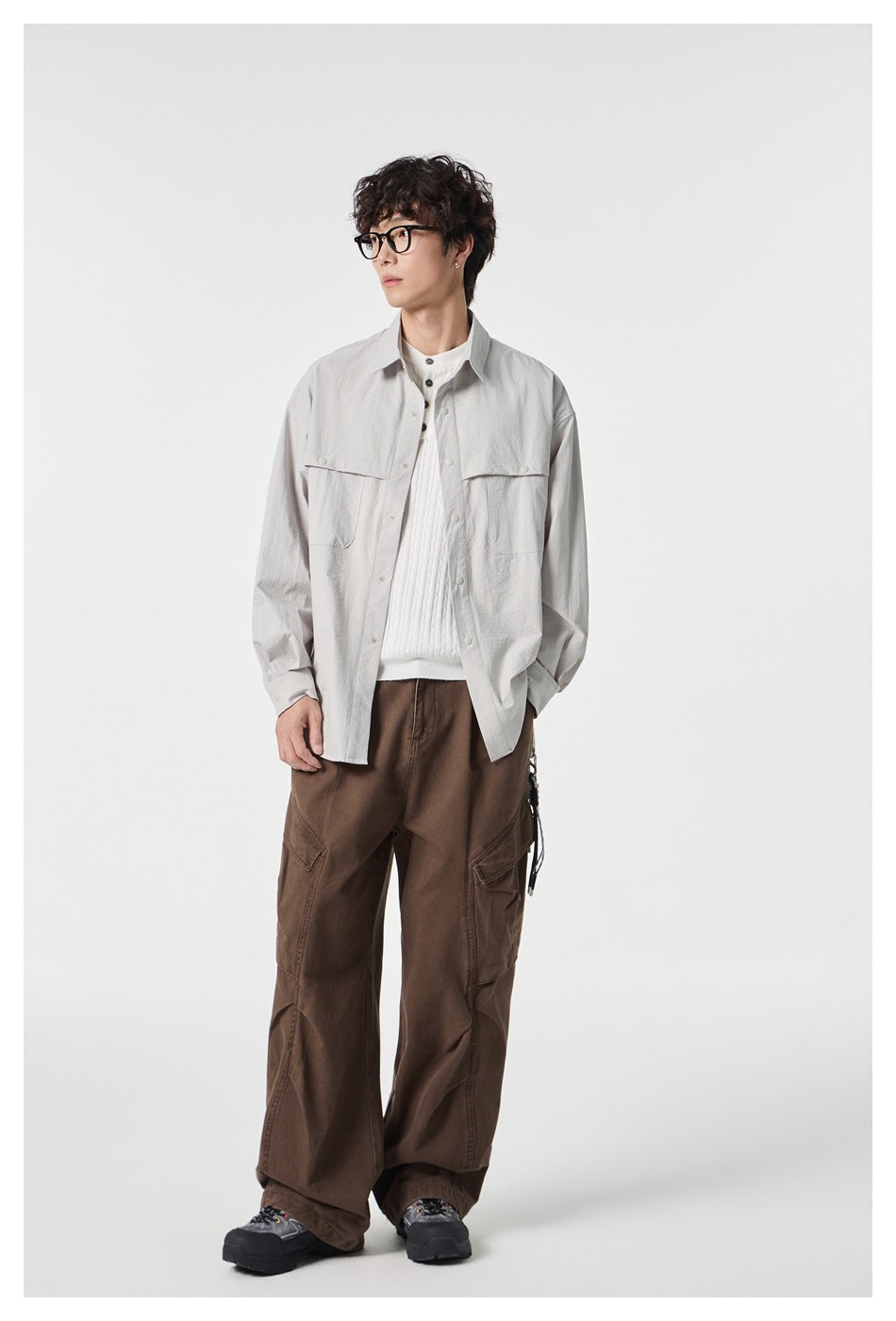 Full-length model wearing a light gray button-front shirt with flap chest pockets and loose brown cargo trousers.