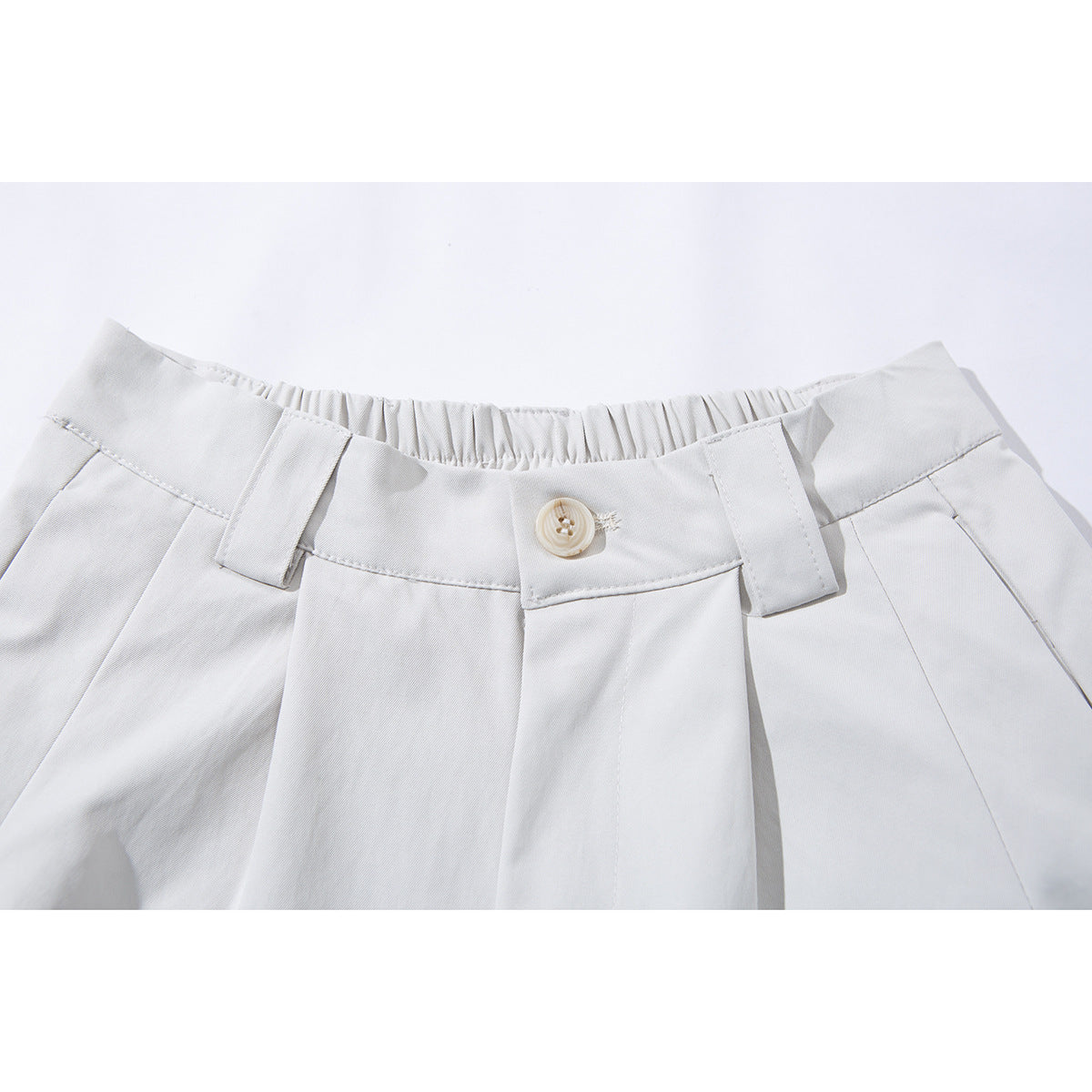 Close-up of white wide-leg shorts showing the elastic back waistband, button, belt loops and front pleats.