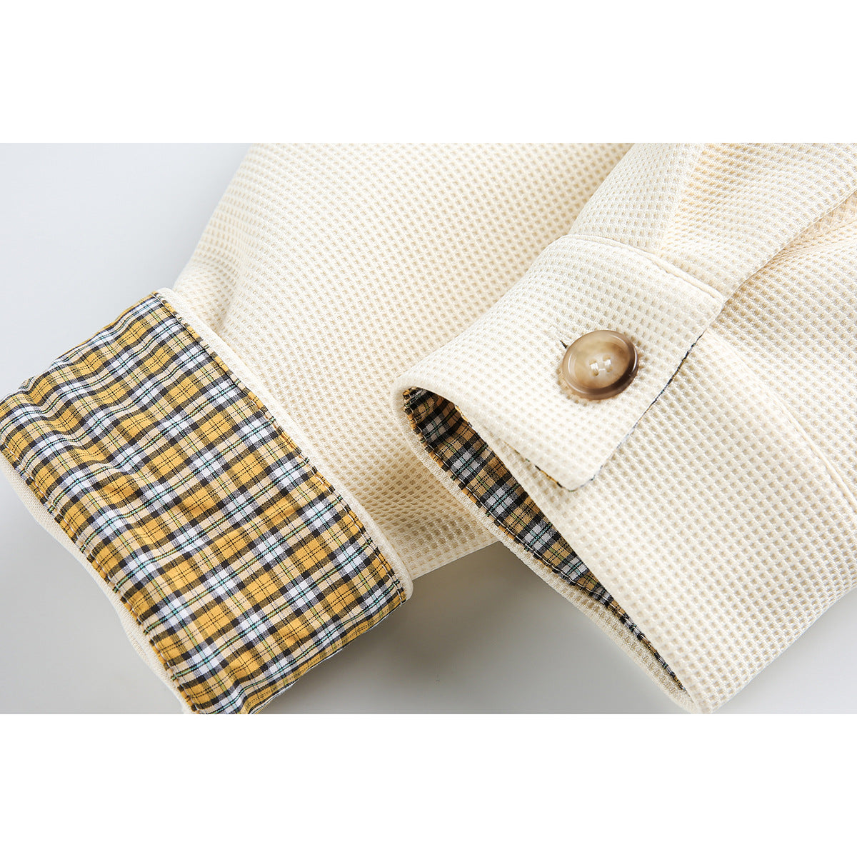 Cream jacket sleeve with a rolled cuff revealing yellow, black, and white plaid lining and a button tab.