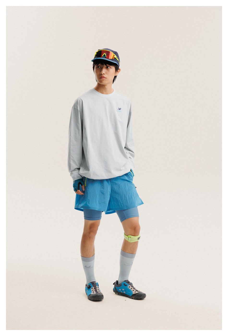 Full-body view of a model wearing a light gray long-sleeve shirt and bright blue shorts.