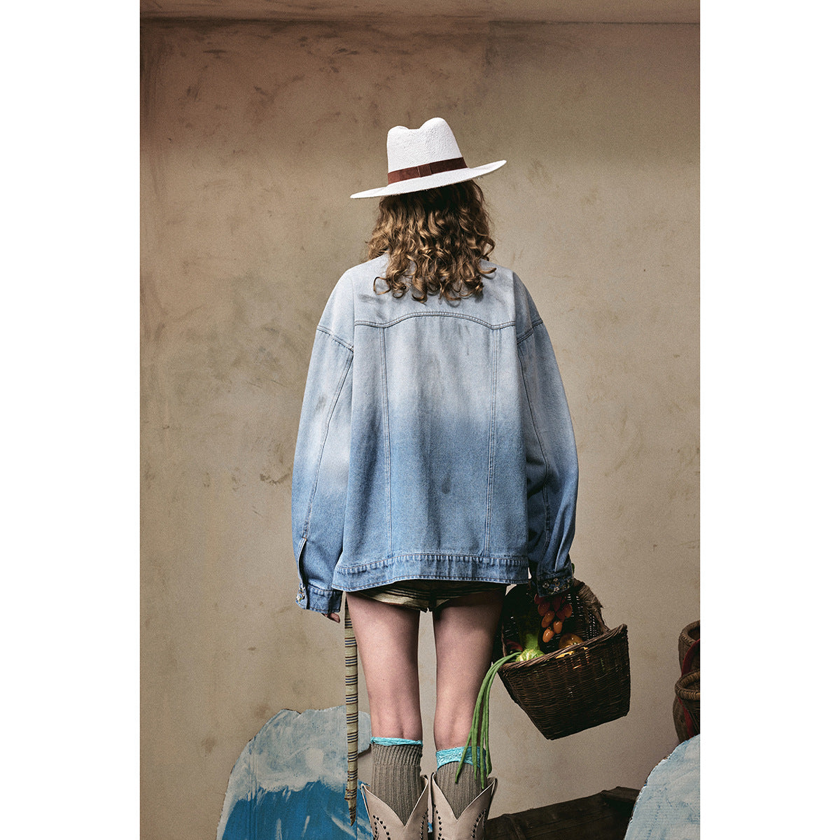 Back view of a model wearing an oversized light blue denim jacket with a plain back and floral cuff details.