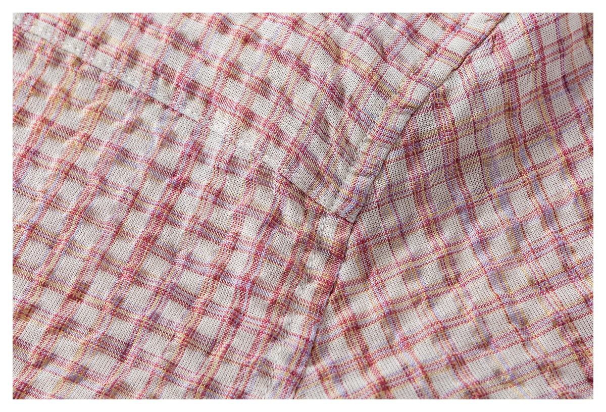 Close-up of a stitched seam joining panels of cream fabric in a pink, red, and muted yellow plaid.