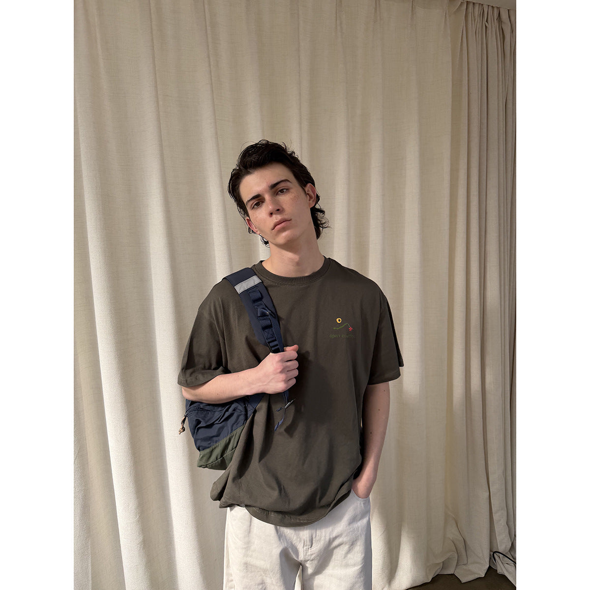 Front view of a person wearing a dark olive T-shirt with a small colorful chest graphic.