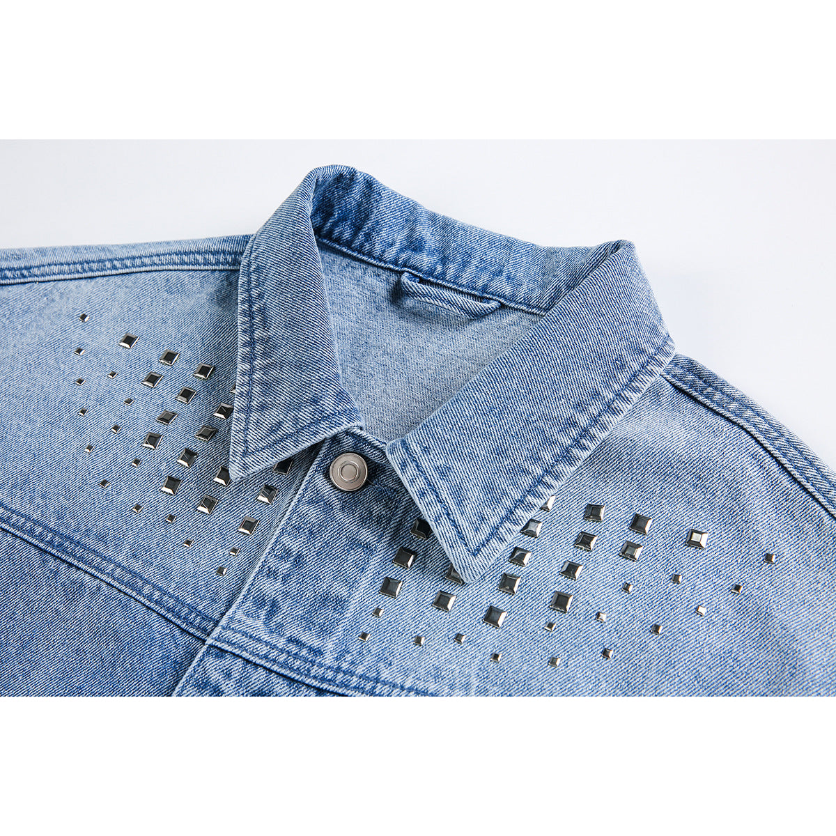Close-up of a light blue denim jacket collar and chest with scattered dark square metal studs.