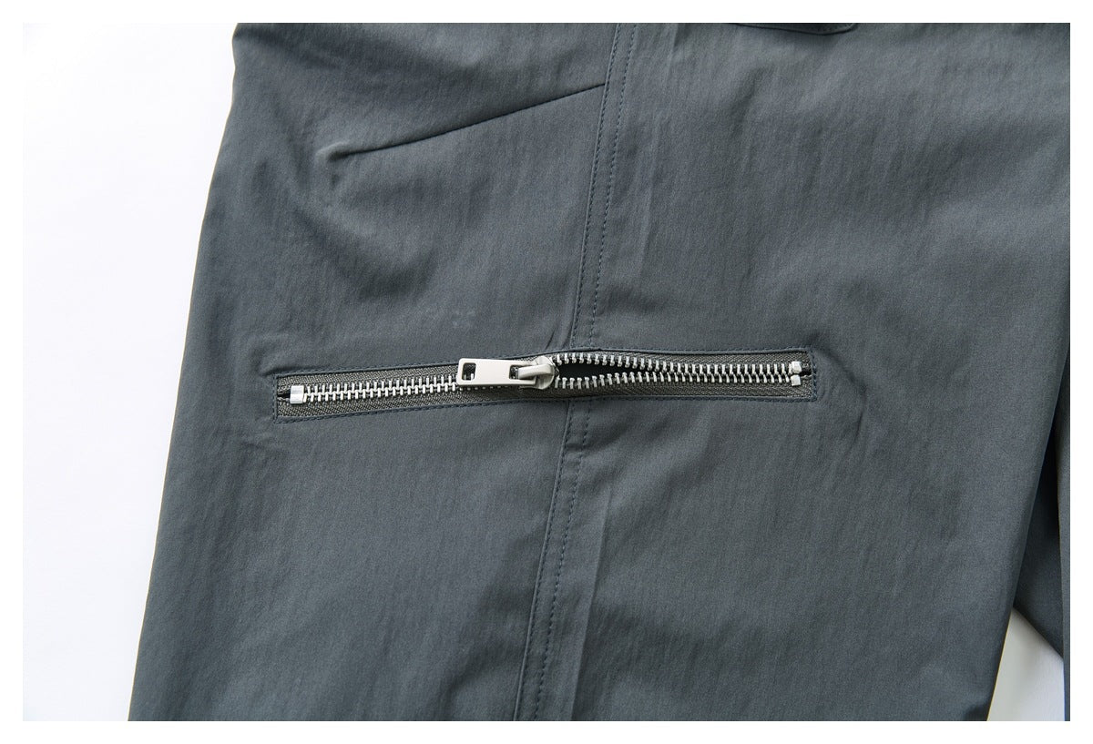 Close-up of charcoal-gray trousers with a horizontal silver zipper pocket and visible stitching.