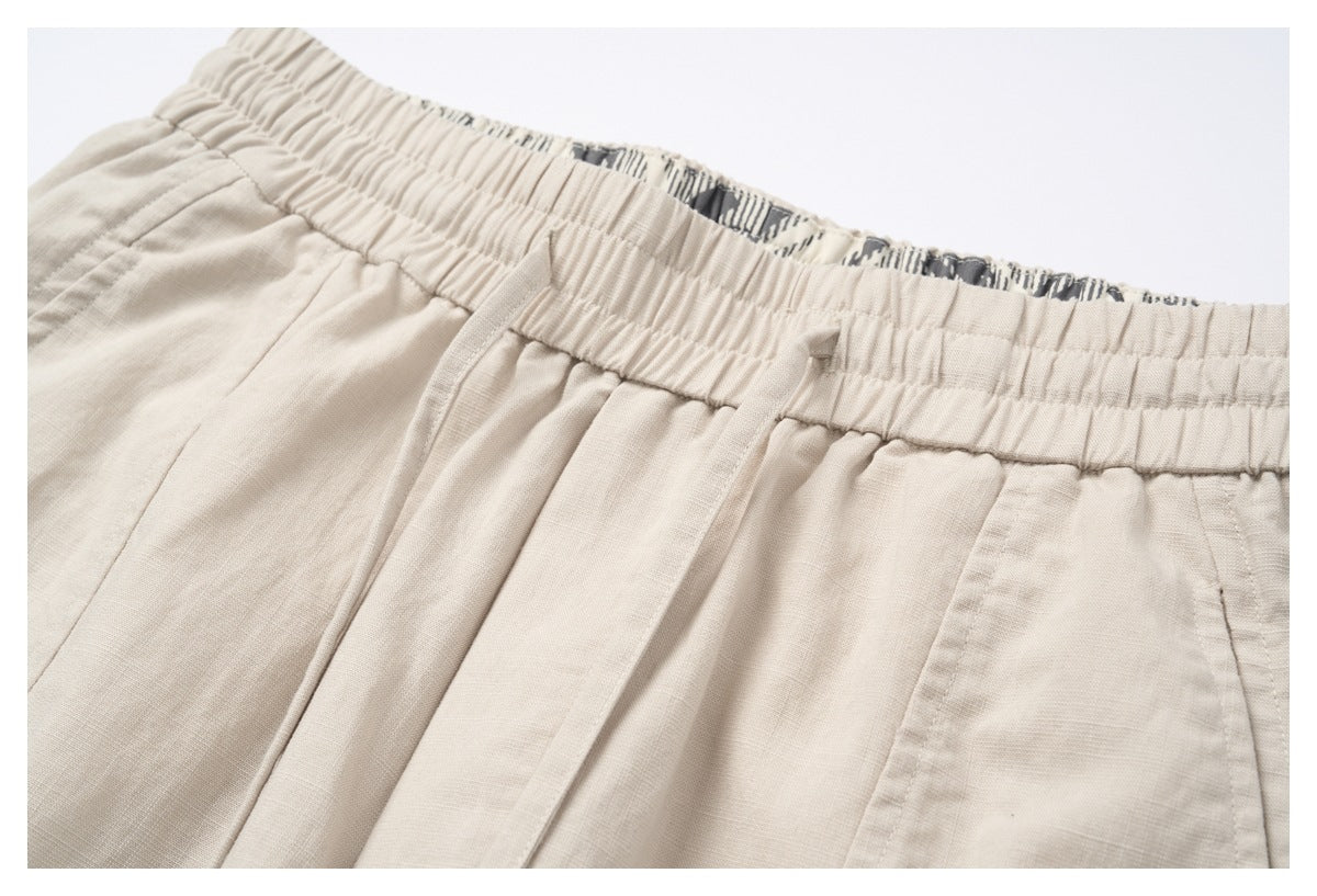 Angled close-up of light beige shorts with a gathered waistband, front pleats and patterned inner facing.