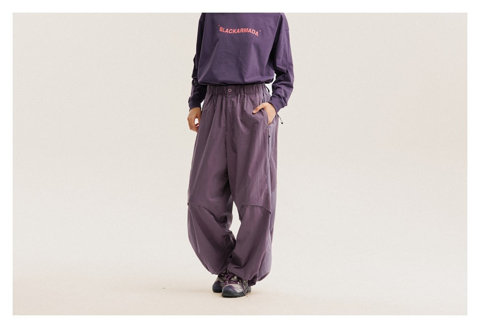 Model wearing loose plum-purple pants with an elastic waist and curved knee panels, shown from a slight angle.