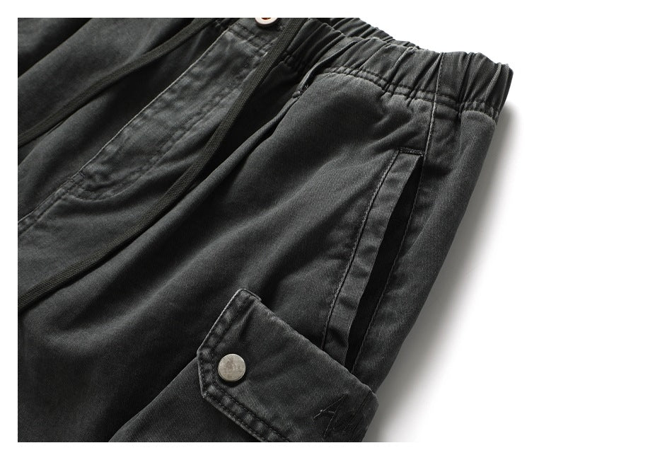 Close-up of charcoal shorts showing the elastic waist, side pocket opening, and snap-button cargo pocket flap.