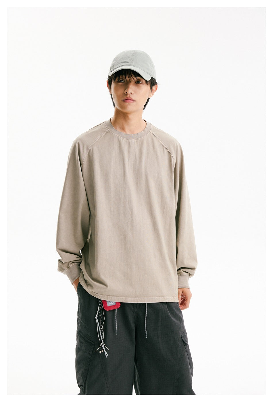 Closer view of a model wearing a plain taupe oversized raglan sweatshirt with dark cargo pants and a light cap.