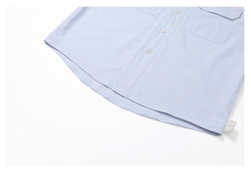 Partial view of a blue-and-white striped shirt front, chest pocket, buttons, and curved hem.