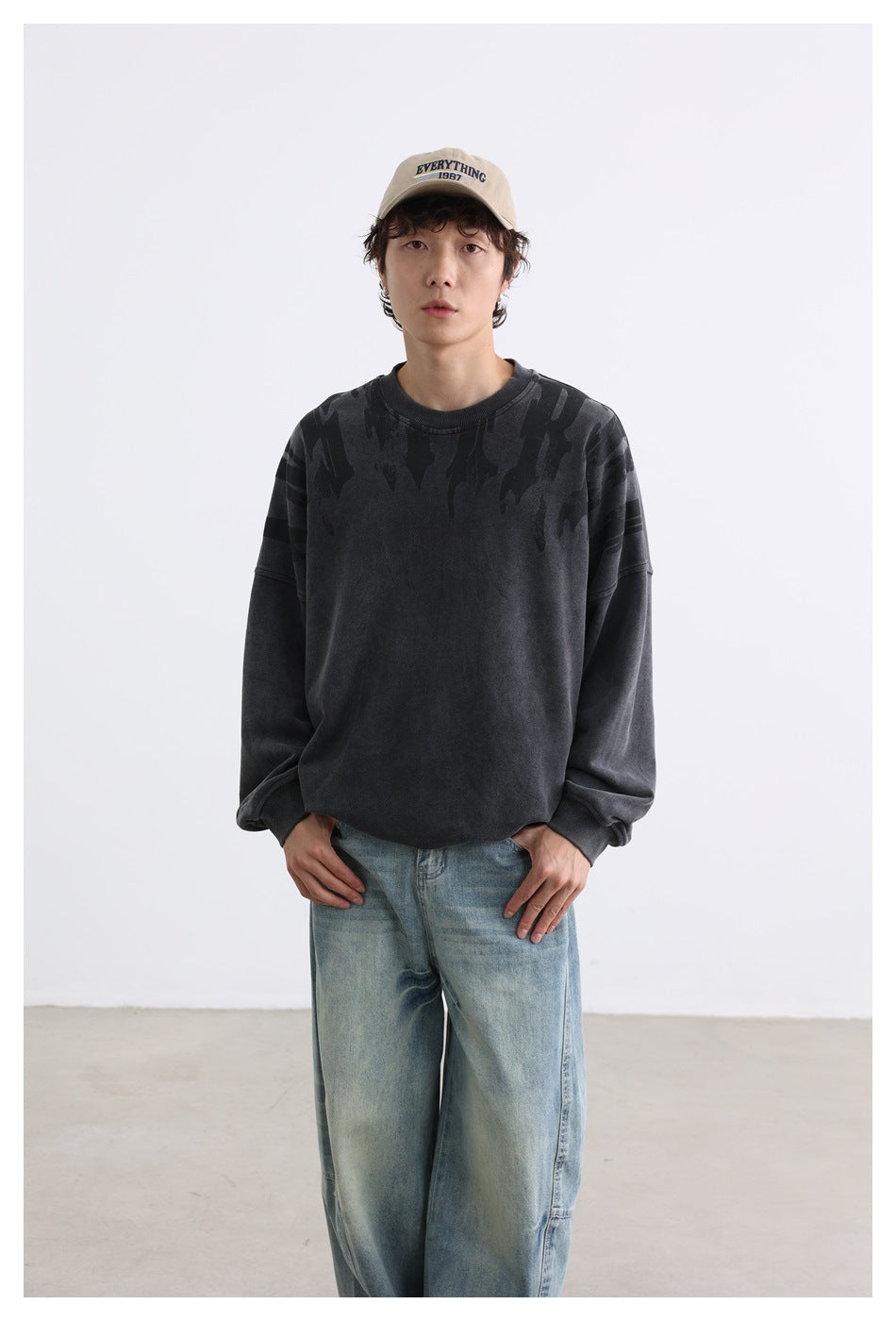 Front view of a model in a charcoal oversized crewneck sweatshirt with dark shoulder graphics and blue jeans.