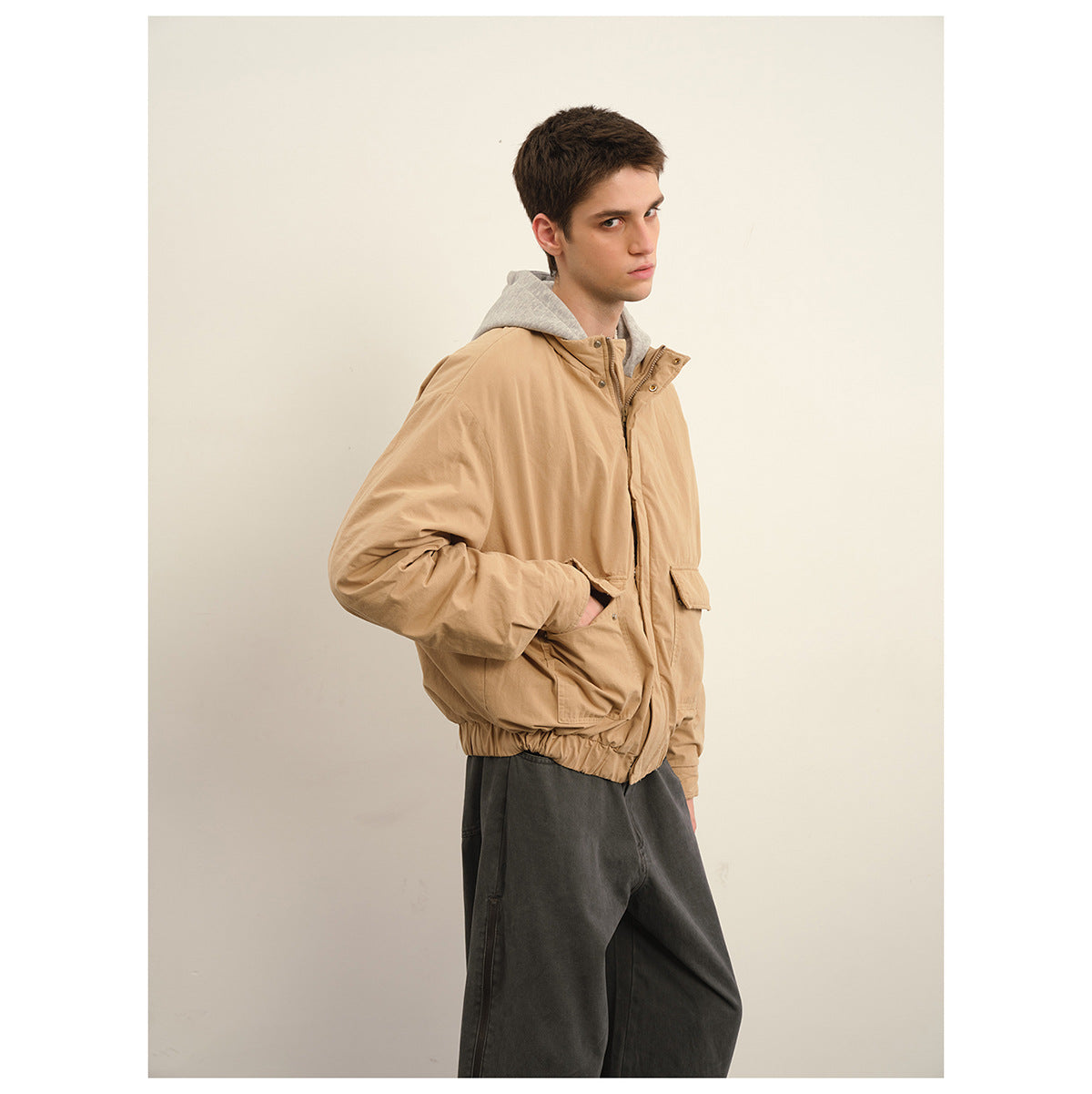 Model wearing a tan hooded jacket with flap pockets and dark gray wide-leg pants.