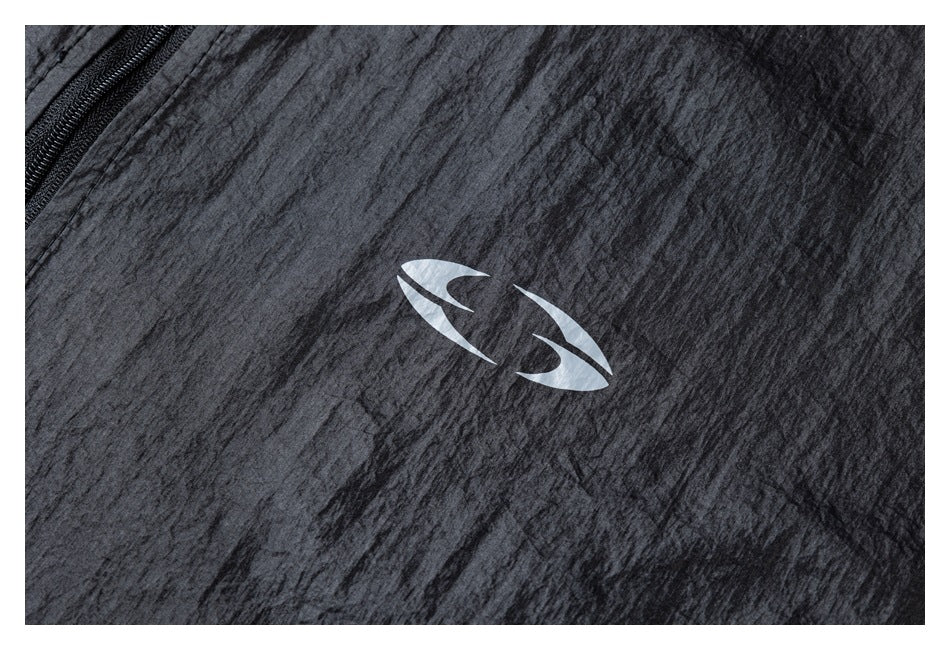 Close-up of a small light-colored emblem on the textured black jacket fabric beside the zipper.