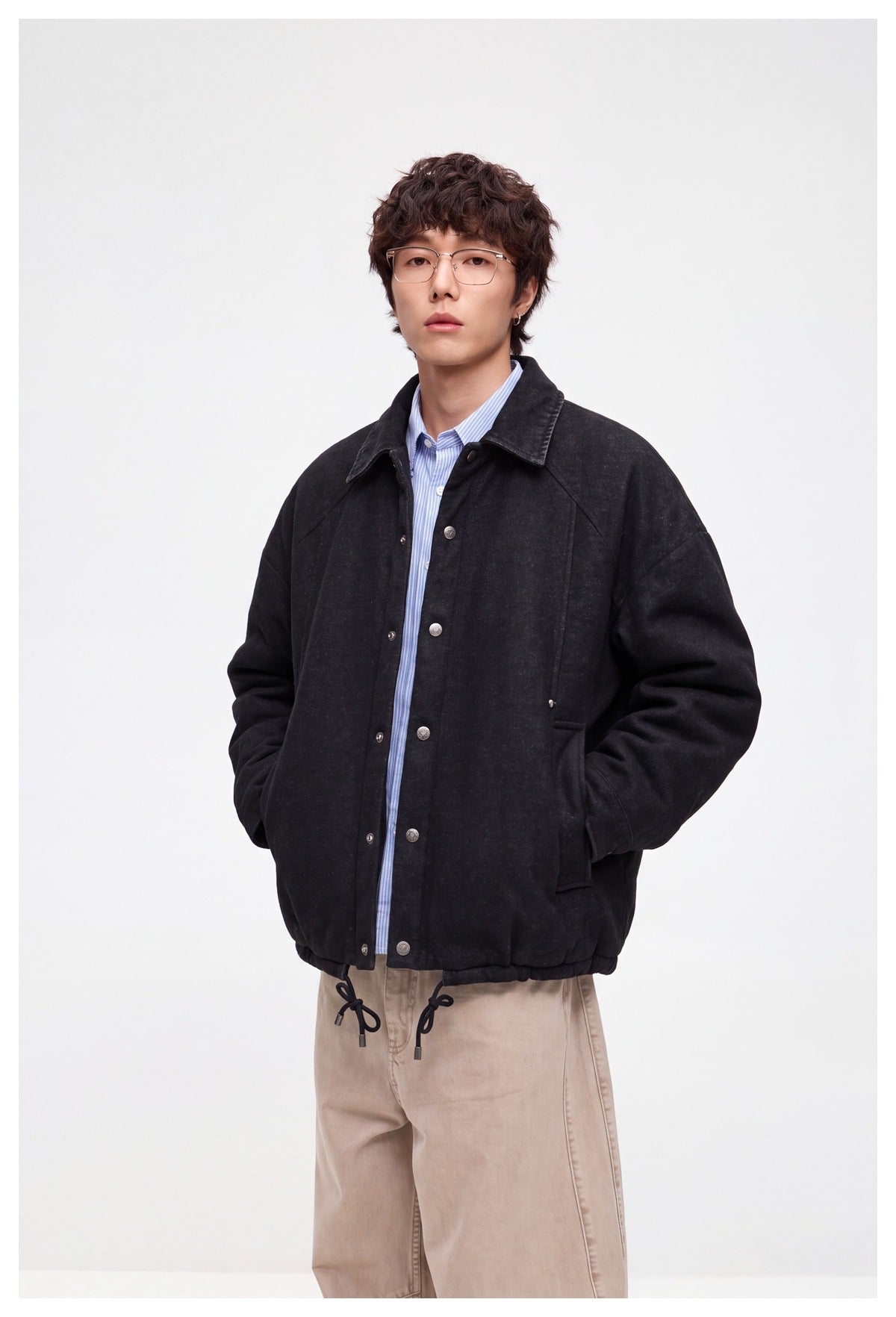 Closer view of a model wearing a black snap-front jacket with a pointed collar and adjustable drawcord hem.
