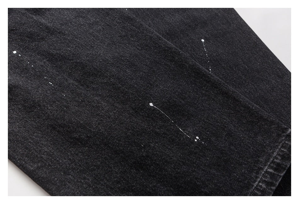 Close-up of black denim fabric with scattered white paint-like splatters and a diagonal seam.