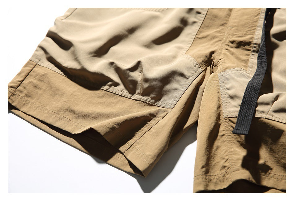 Close-up of tan shorts showing stitched panel seams and a black webbing strap.