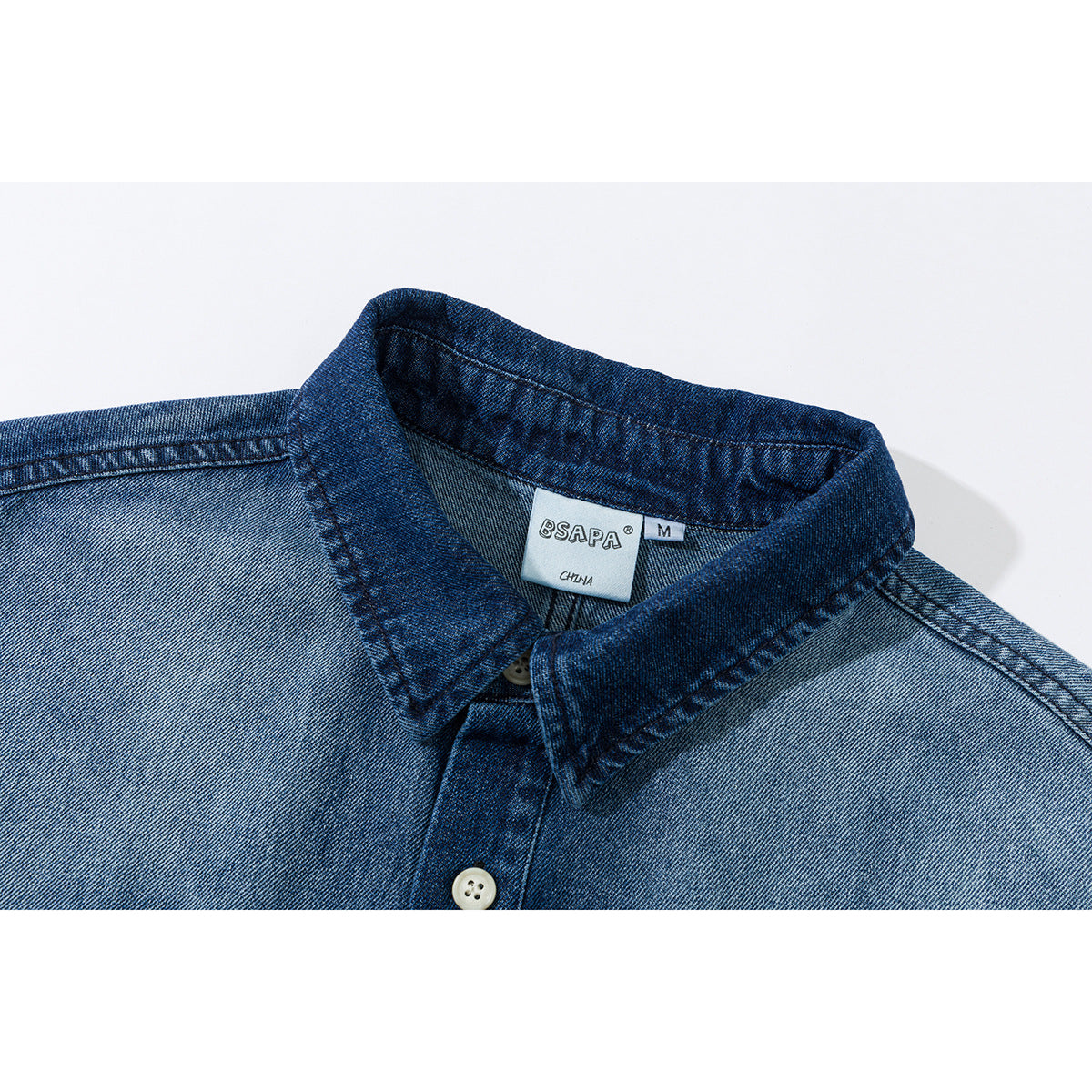 Close-up of a blue denim shirt collar, upper placket and white buttons, with a visible neck label.