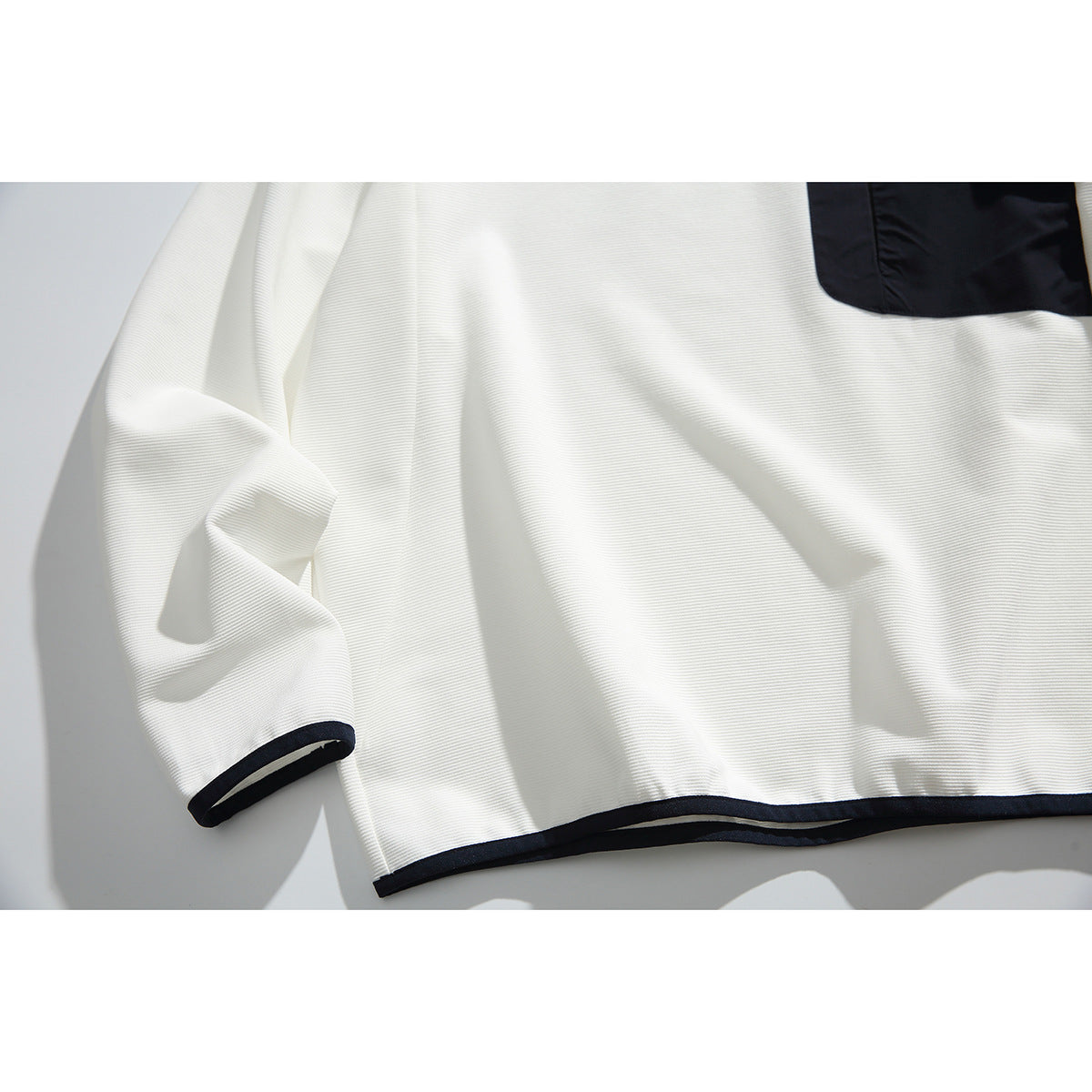Close-up of the off-white sweatshirt's navy-trimmed hem and cuff, with part of the navy chest pocket visible.
