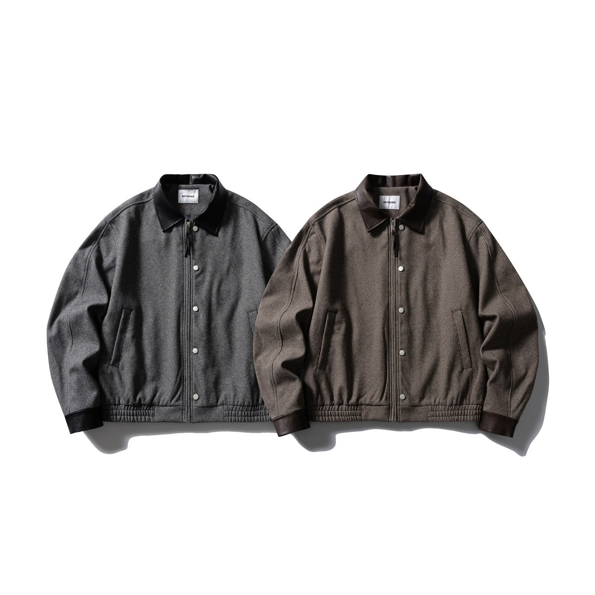 Two jackets shown from the front: one charcoal gray and one brown, both with dark collars, cuffs, and snap closures.