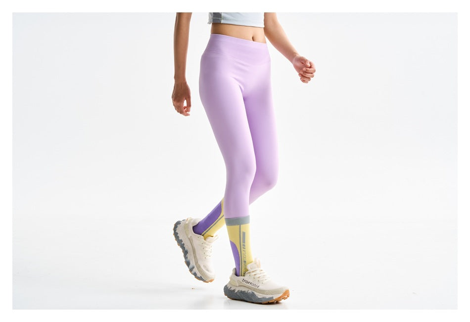 Cropped view of a model walking in lilac full-length leggings, color-block socks and sneakers.