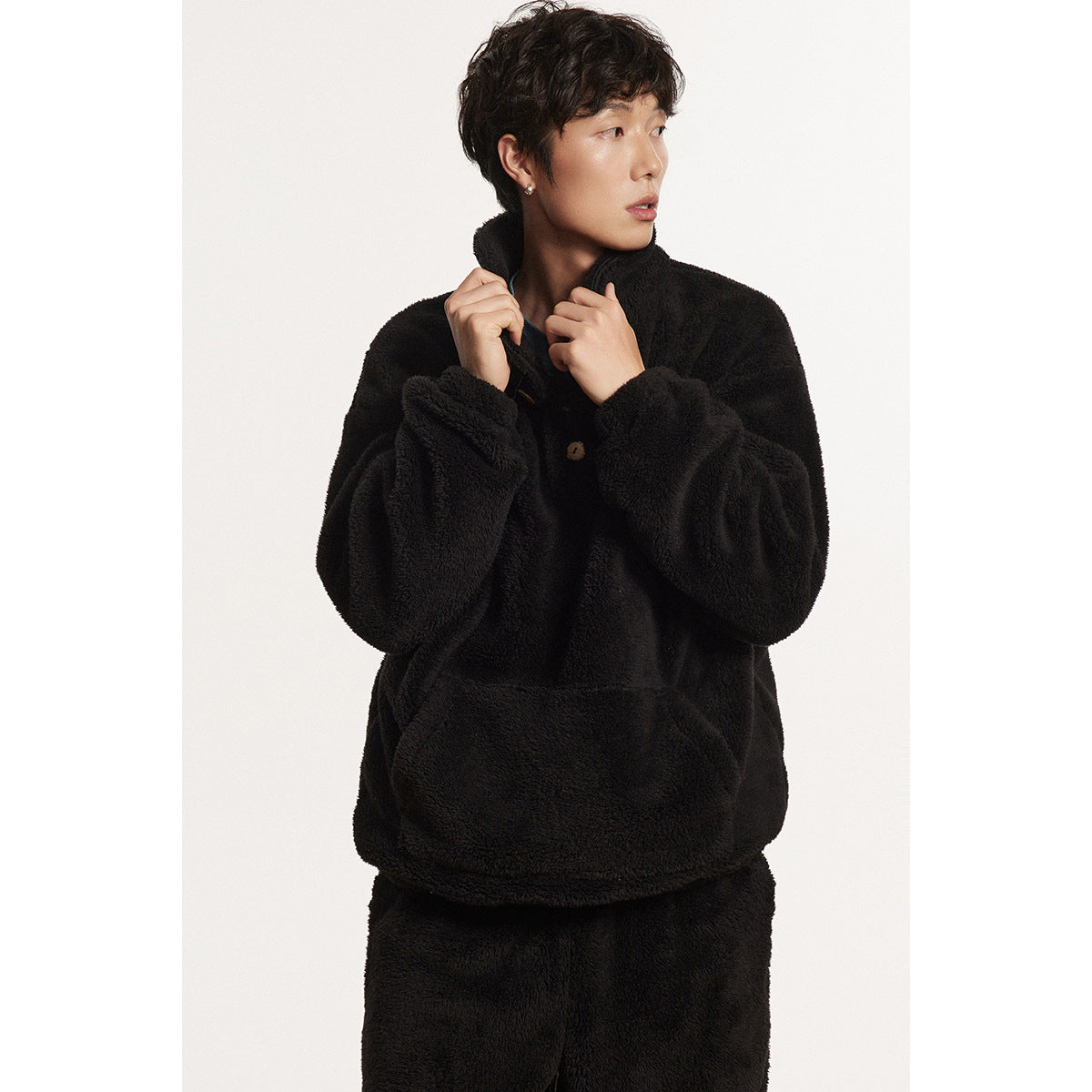 Model wearing a black plush pullover with a wide collar, button placket and kangaroo pocket.