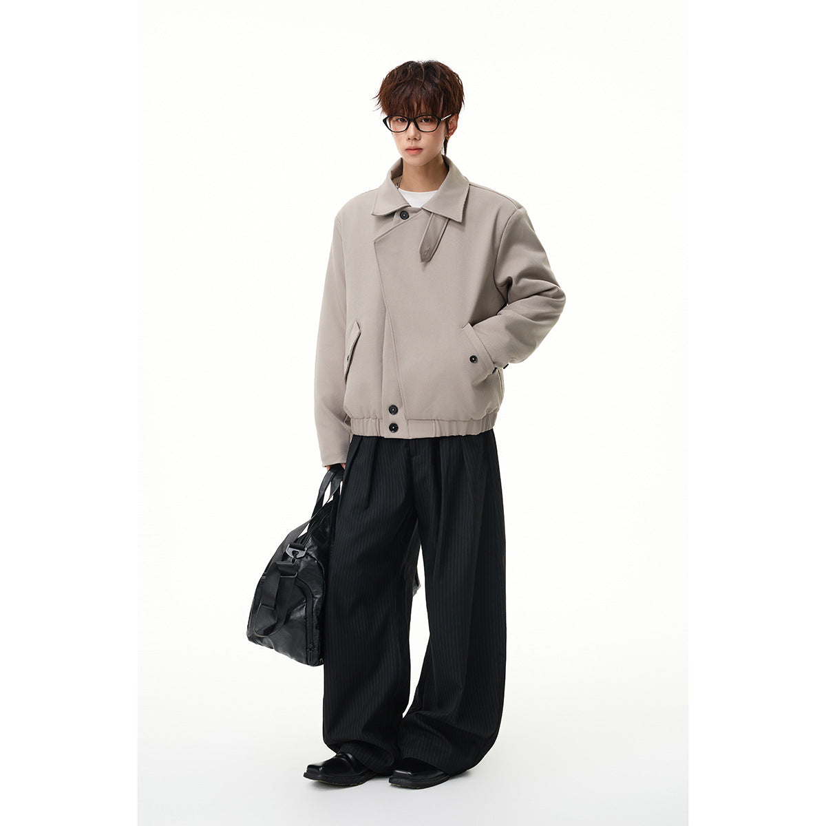 Full-length model wearing a taupe buttoned jacket with black pinstripe trousers and carrying a black bag.