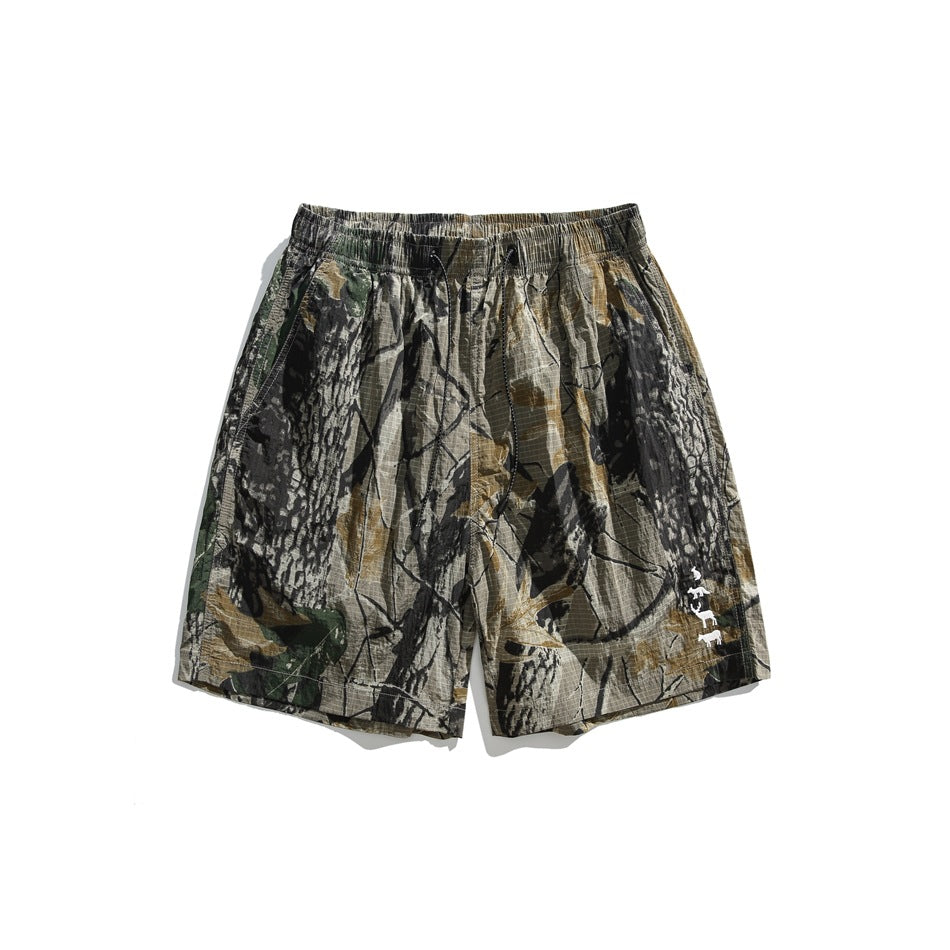 Khaki and olive tree-branch camouflage shorts with elastic drawstring waist and small white animal motif, front view