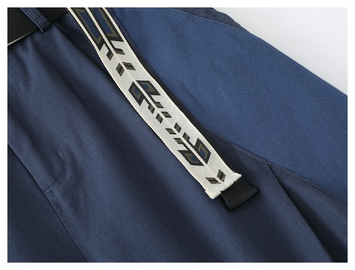 Close-up of blue trousers showing the cream geometric-patterned belt end and a stitched pocket seam.