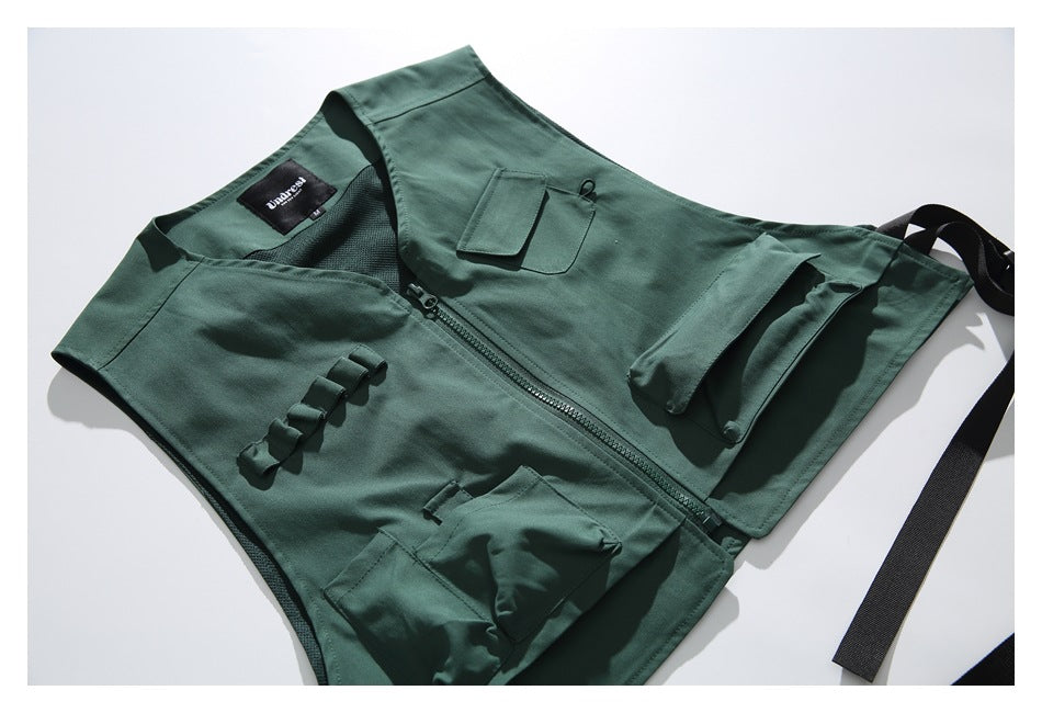 Dark green utility vest laid diagonally, showing its front zipper, multiple pockets, webbing loops, and black straps.