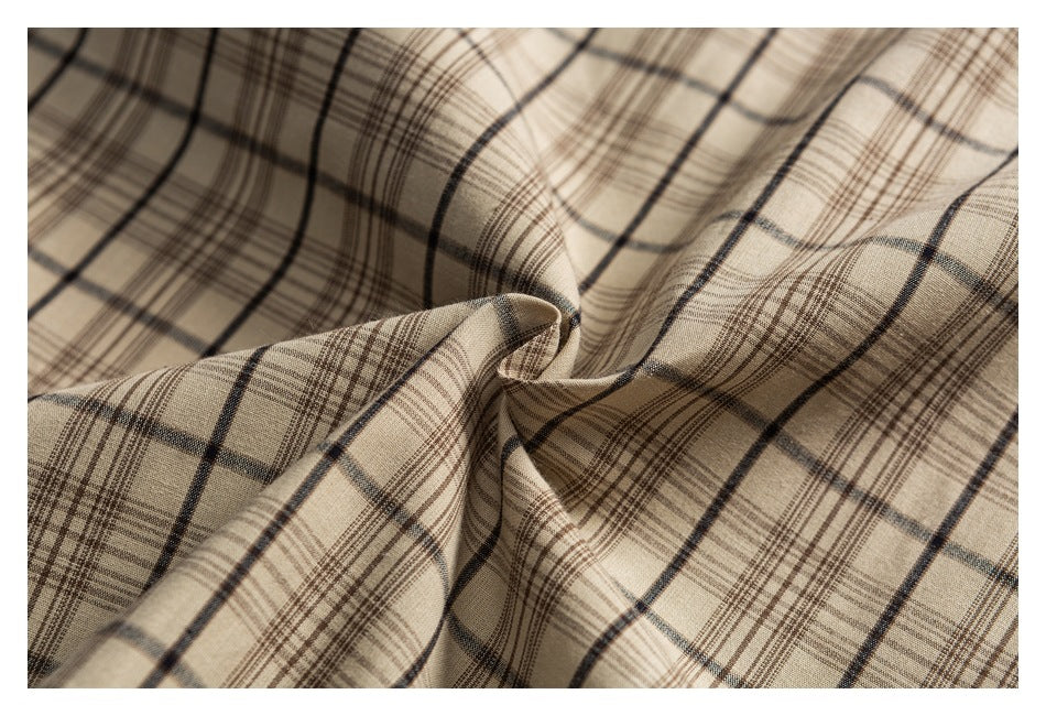 Close-up of beige fabric with a dark brown and black plaid pattern, gathered into soft folds.