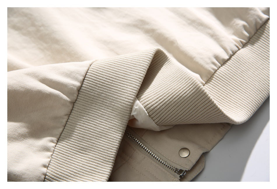 Close-up of the beige jacket's ribbed trim, zipper, and snap fastener.