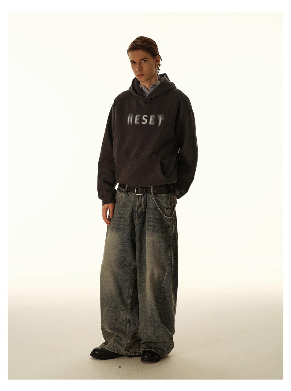 Full-length view of model in dark gray RESET print hoodie, belt with chain and wide-leg washed jeans