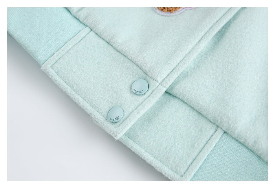 Close-up of two pale mint snap buttons and stitched seams on a coat hem.