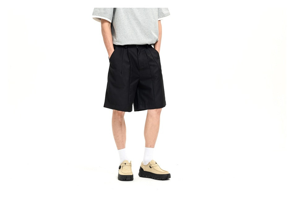 Angled front view of a model wearing black pleated shorts with a gray T-shirt and beige shoes.