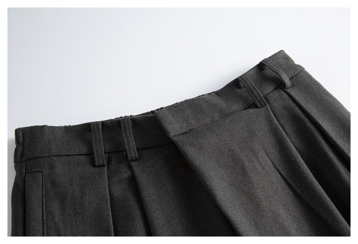 Close-up of the charcoal trousers’ waistband, belt loops, pleats, and pocket opening.