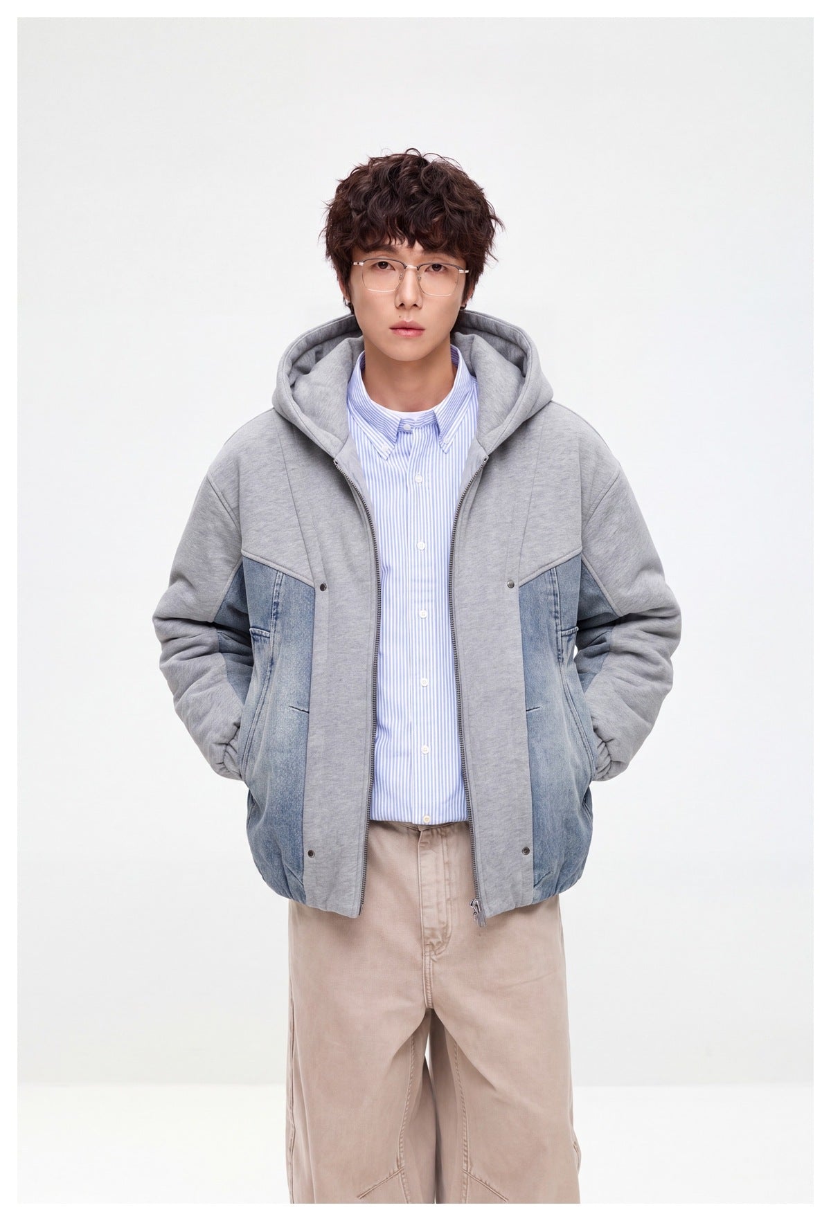 Front view of a model wearing an open gray hooded jacket with blue denim panels over a striped shirt.
