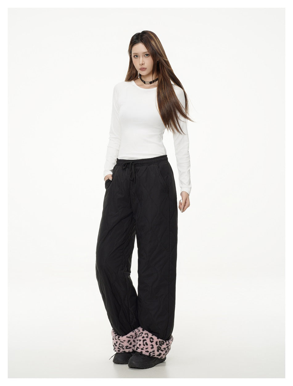 Full-length model wearing black quilted wide-leg pants with pink leopard-print cuffs and a white long-sleeve top.