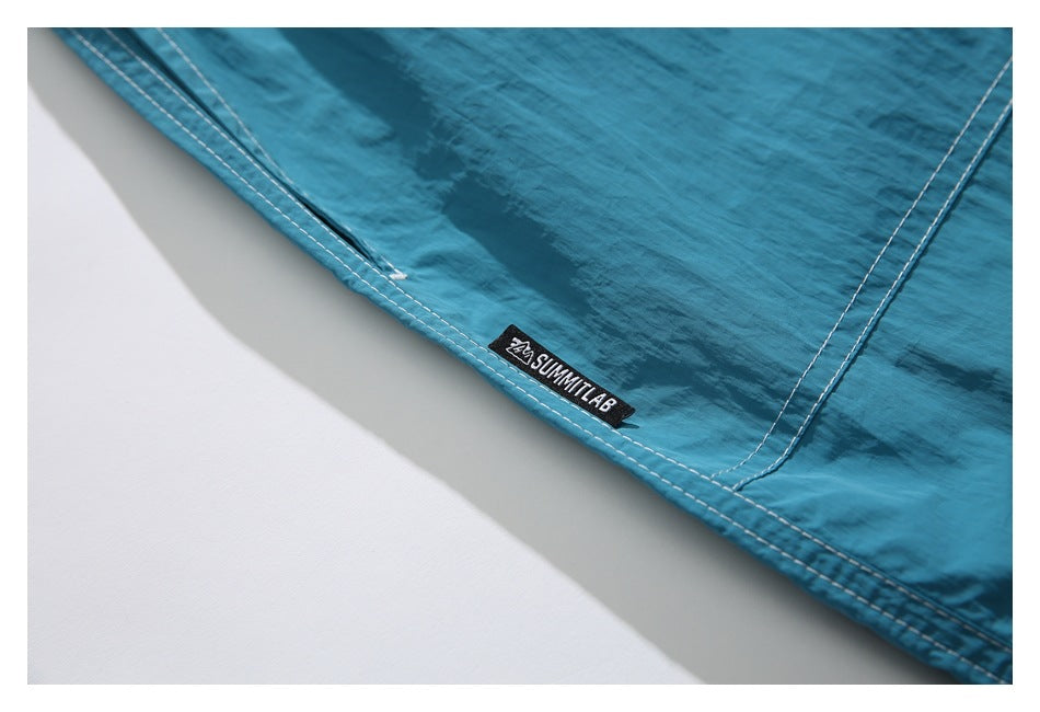 Close-up of the stitched hem and small black SUMMITLAB label on turquoise shorts.