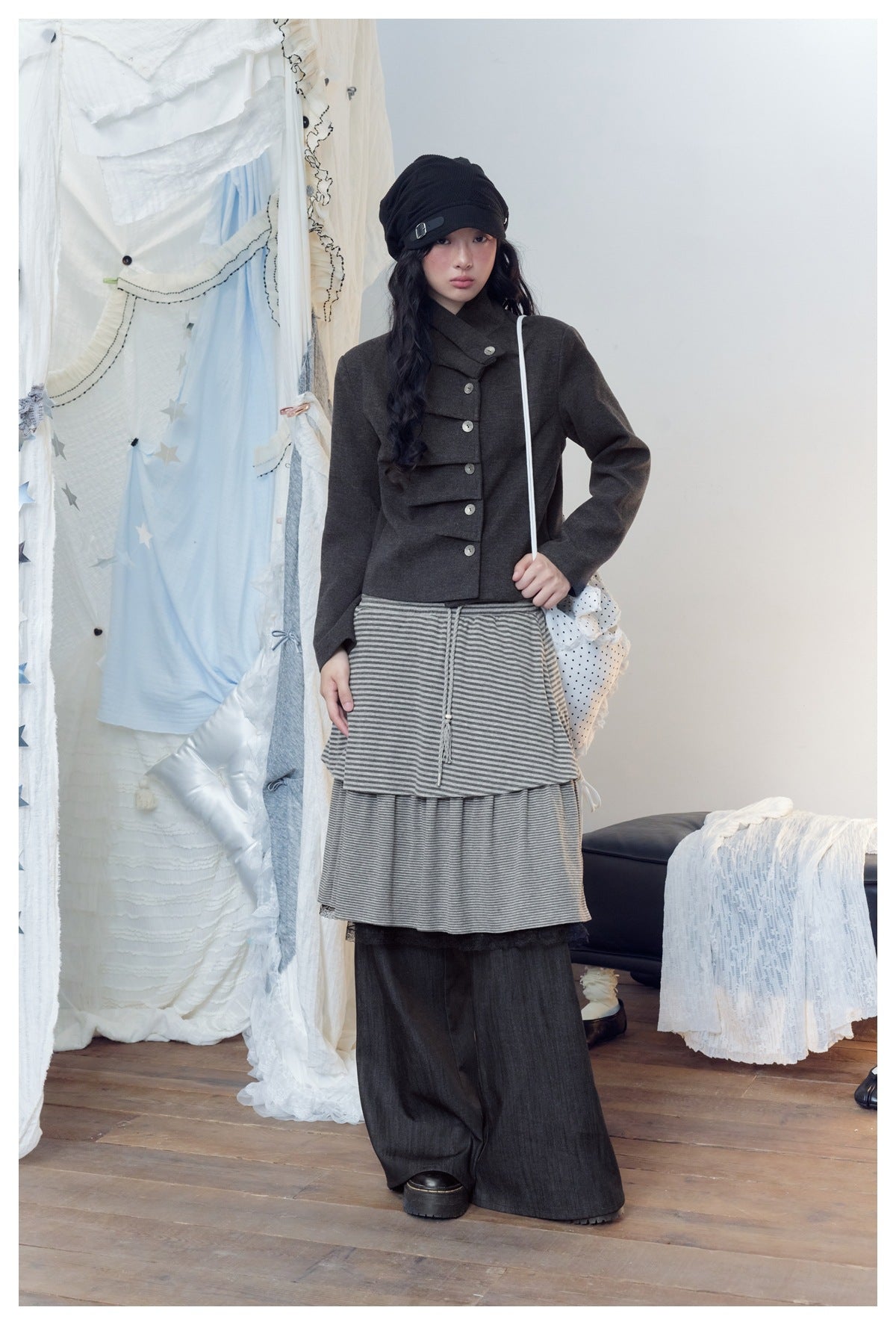 Full-length front view of a model wearing a charcoal jacket, gray striped layered skirt, and wide dark pants.