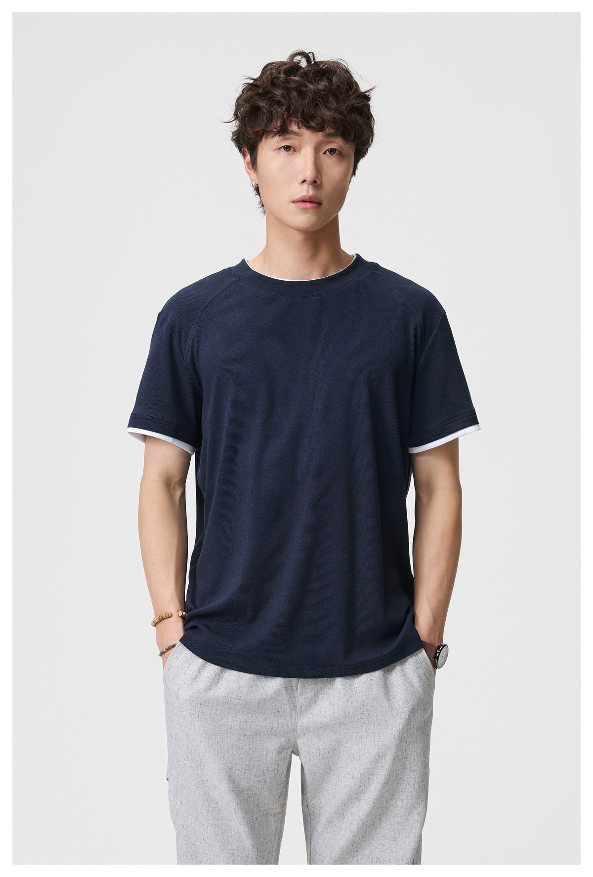Front view of a model wearing a navy crew-neck T-shirt with white sleeve-cuff trim.