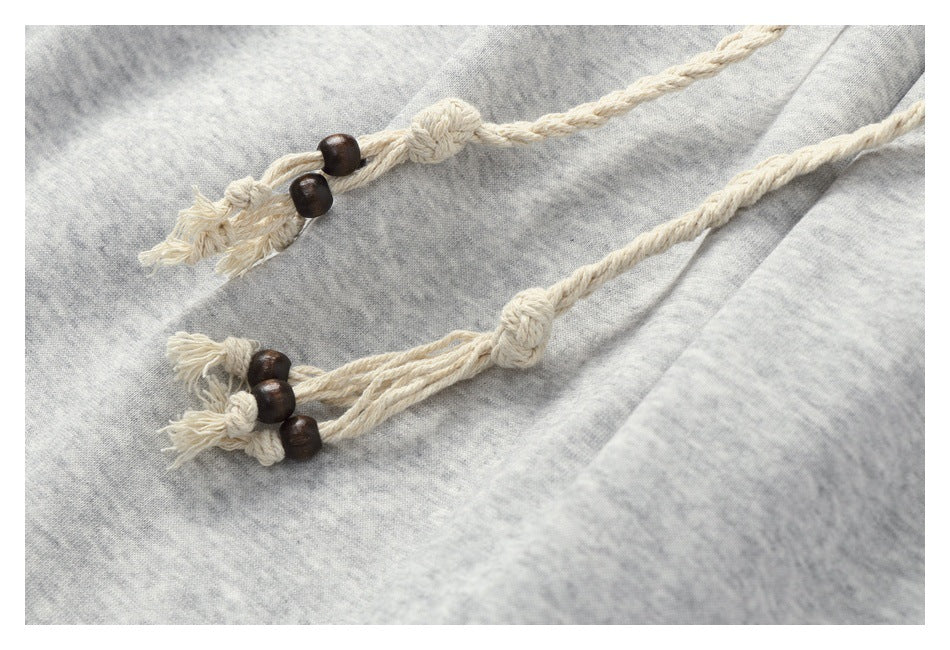 Close-up of cream braided drawstring ends with dark wooden beads against light gray heathered sweatpants.