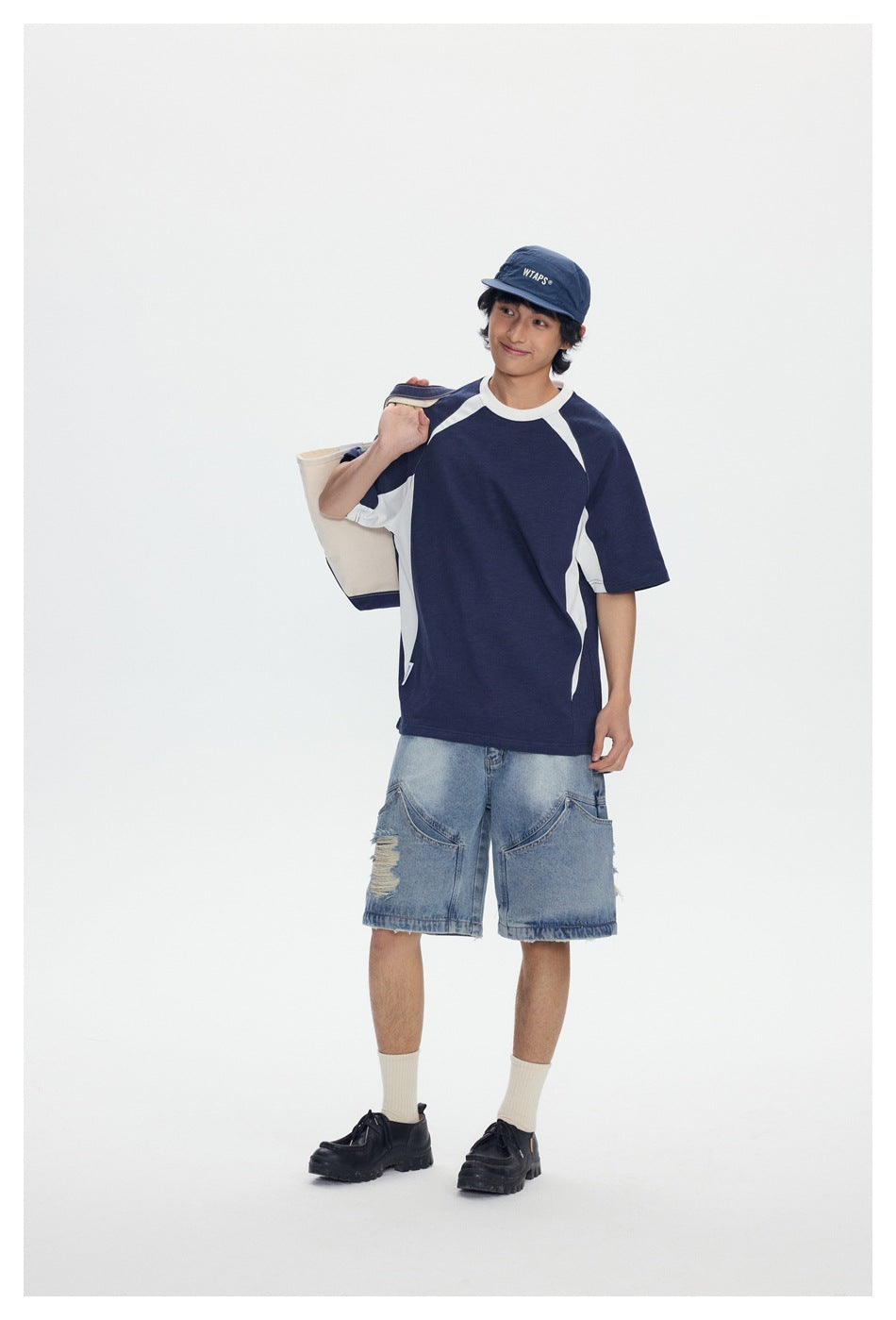 Model wearing a navy and white raglan T-shirt with distressed light-wash denim shorts, shown from the front.
