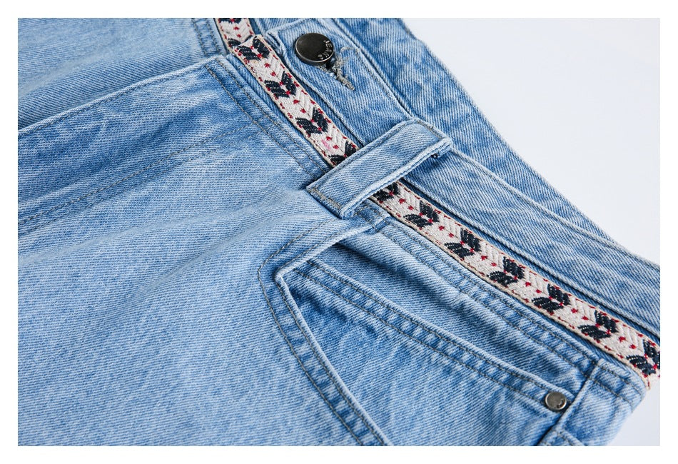 Close-up of light-wash blue jeans showing the waistband, patterned inner trim, button, belt loop and front pocket.