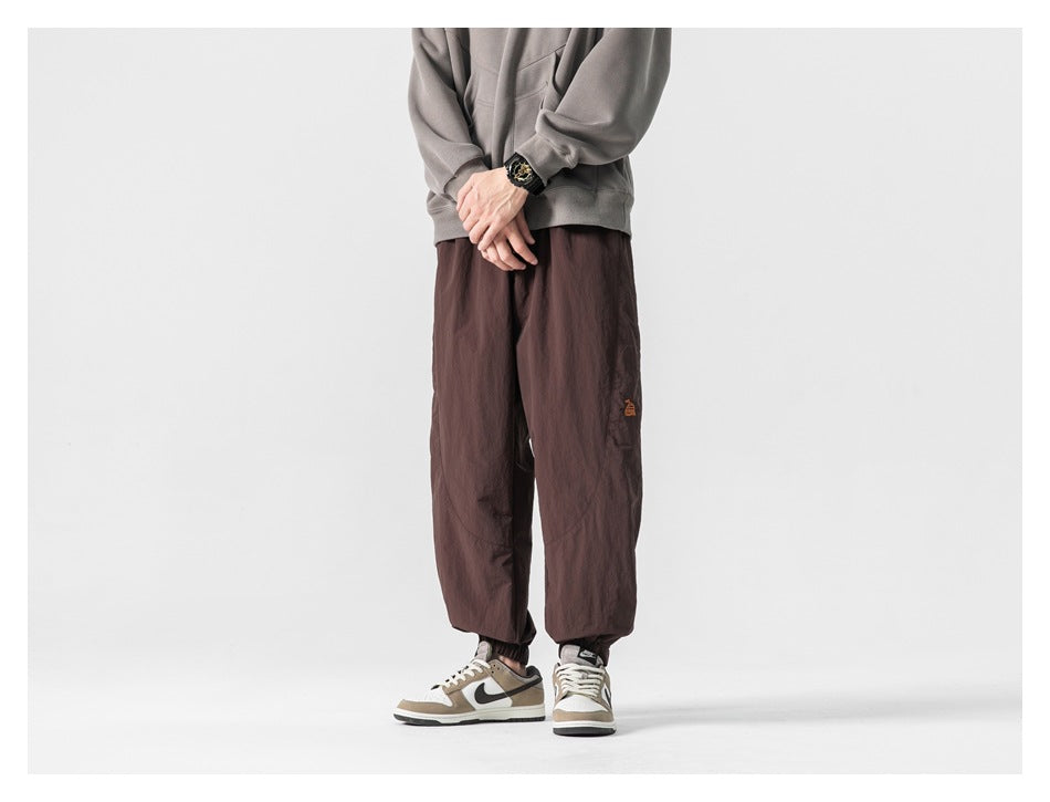Model wearing dark brown loose-fit jogger pants with elastic cuffs and a small embroidered emblem, front view.