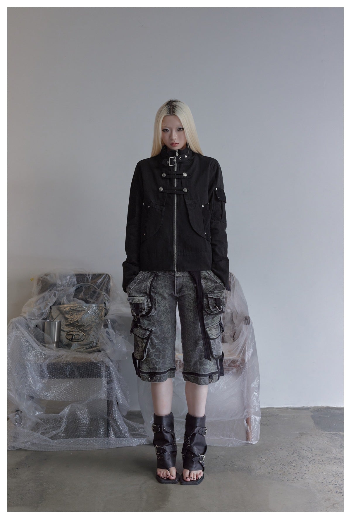 Full-length front view of a model wearing a black high-collar jacket with metal fastenings and gray cargo shorts.