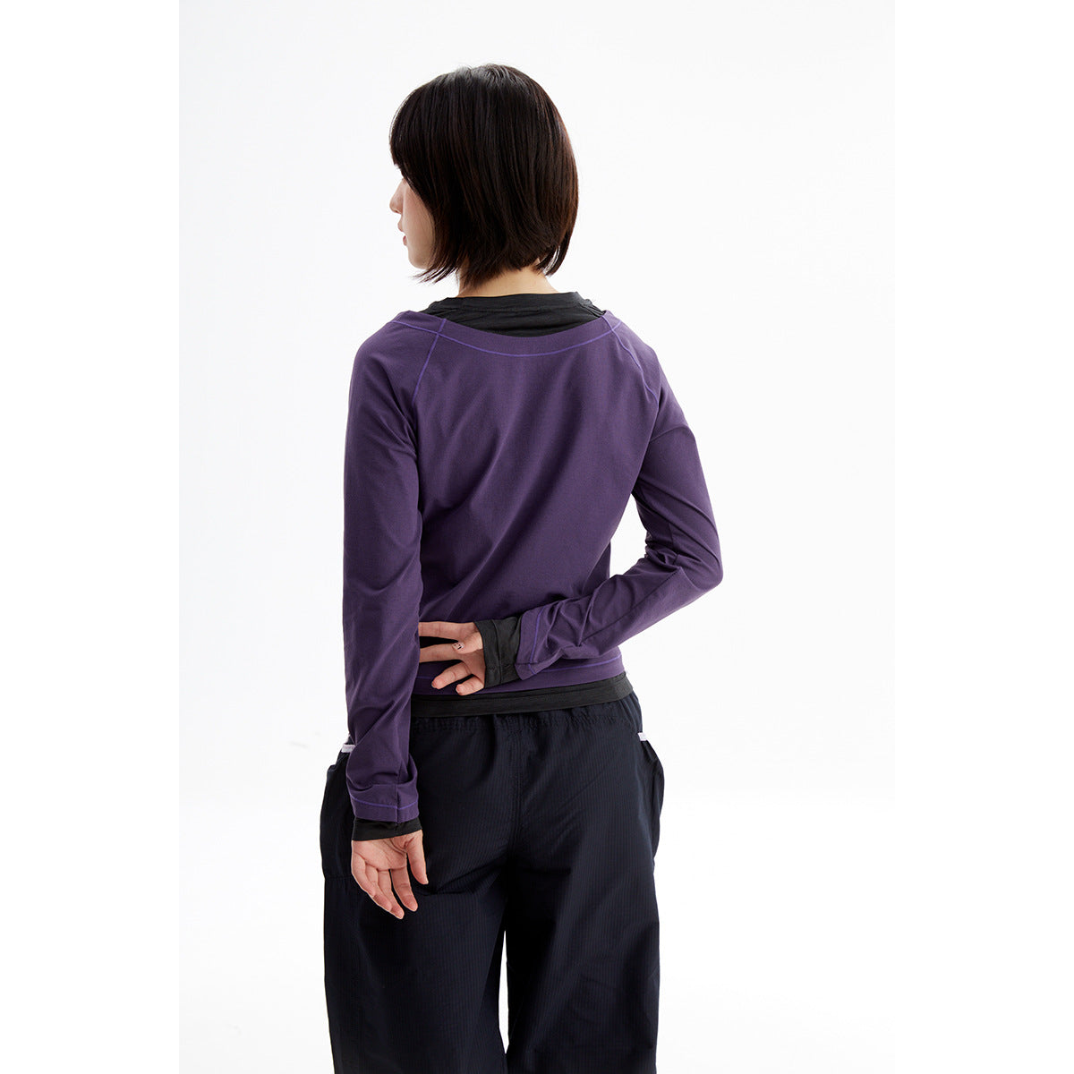 Back view of a model wearing a purple long-sleeve top over a black shirt and black trousers.