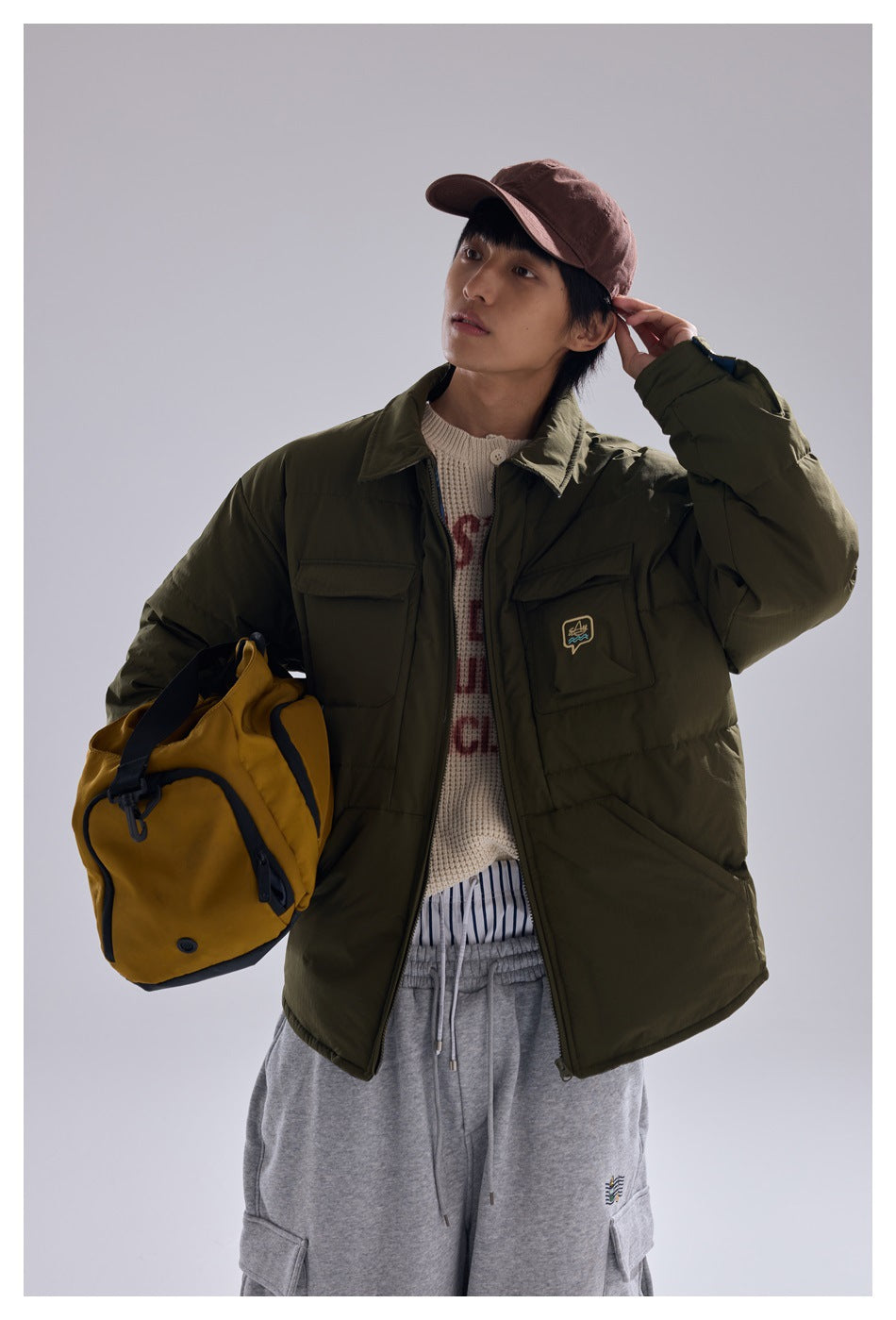 Model wearing an olive quilted jacket with flap chest pockets, holding a mustard-yellow bag.