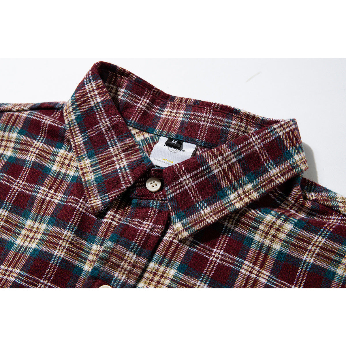 Close-up of a burgundy, teal, and cream plaid shirt collar, placket, and neck label.