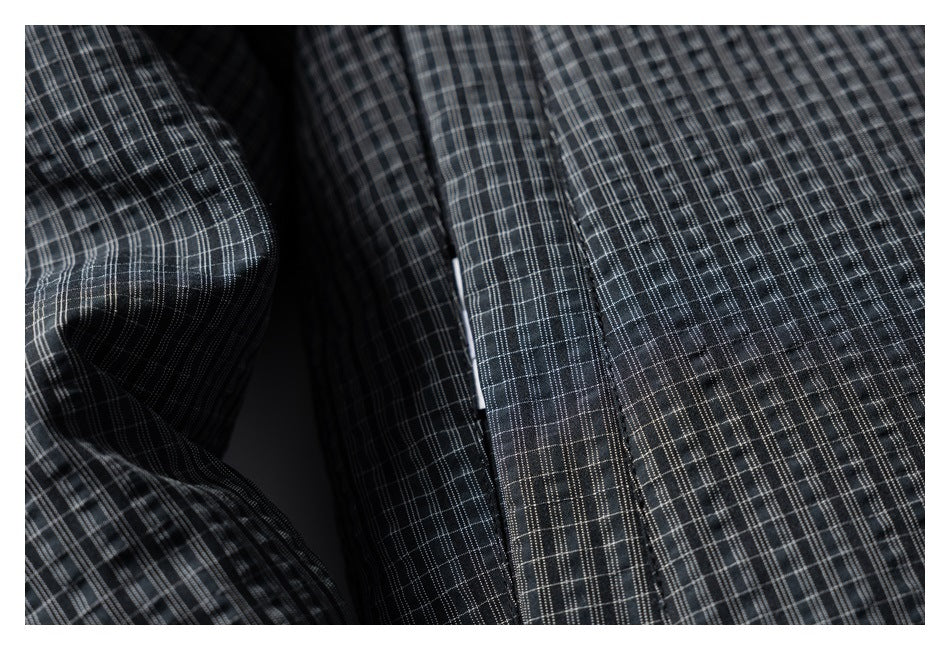 Close-up of charcoal plaid fabric with a stitched front placket and a glimpse of a light-colored fastener.