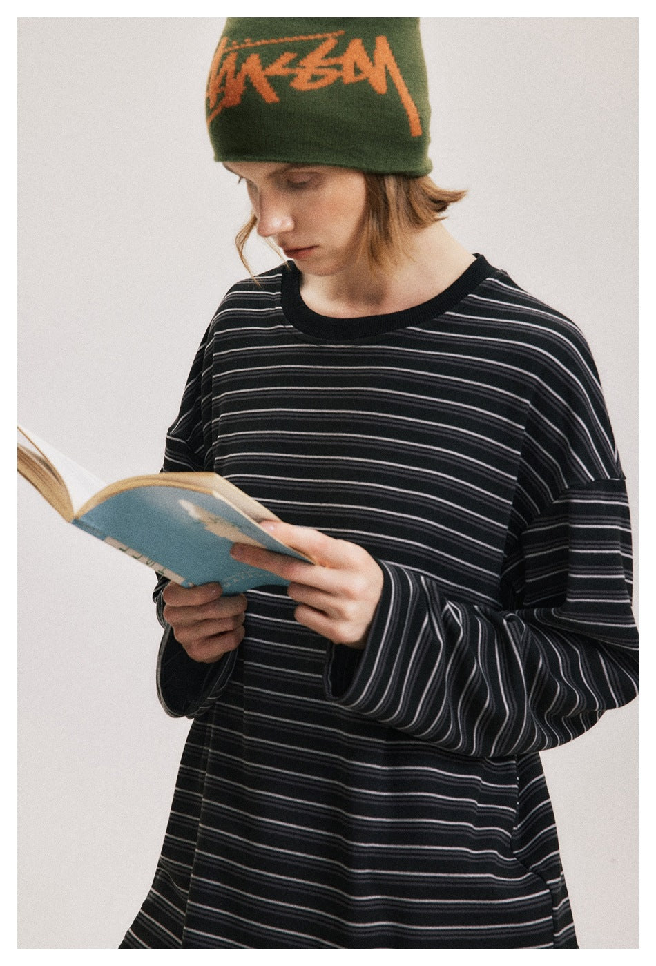 Person wearing a loose black striped long-sleeve shirt, shown from the front while reading.